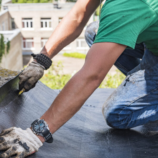 A construction worker cuts waterproofing material and prepares it for installation. Overhaul of the roof of the house.